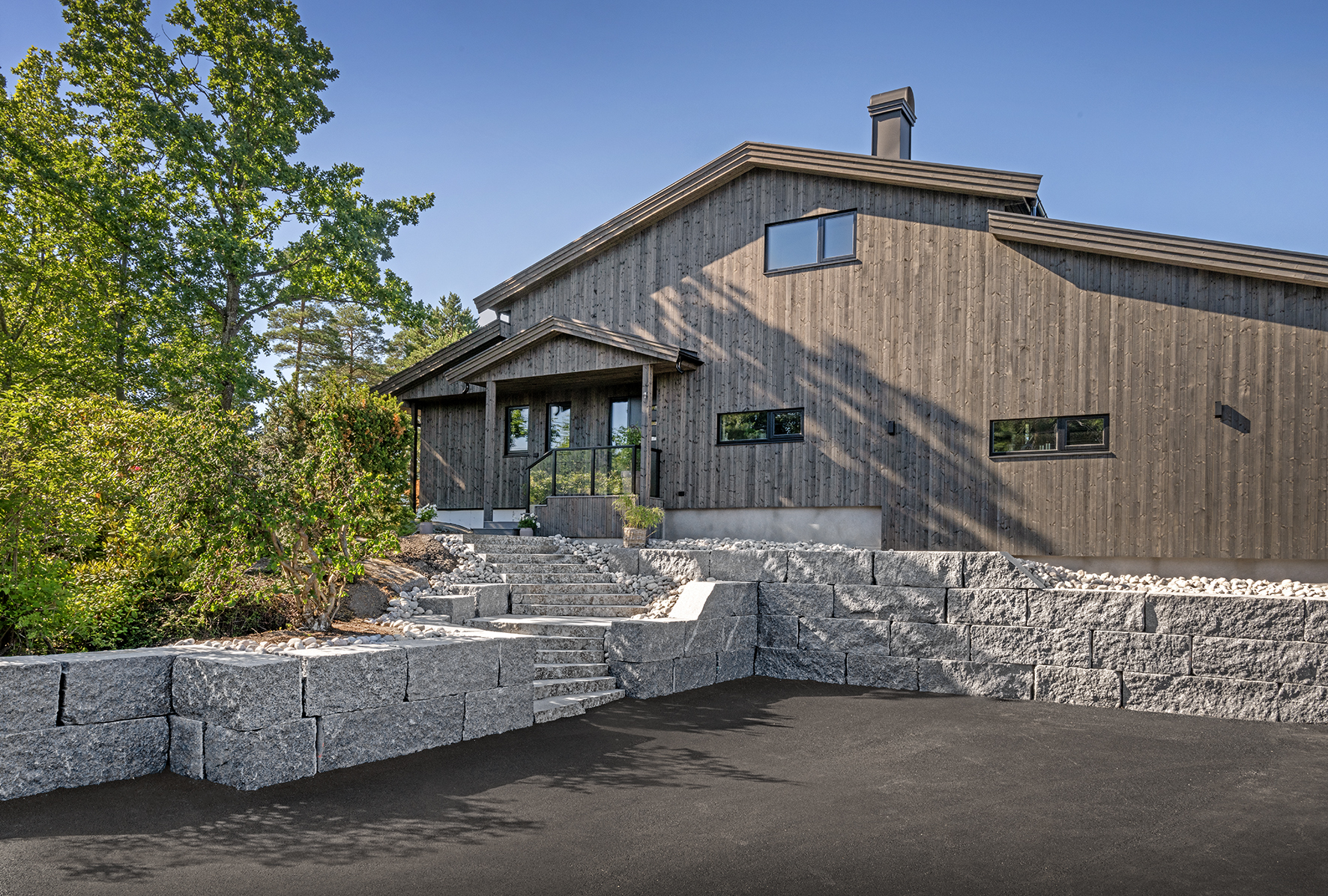 Moderne, brunt hus med gårdsplass innrammet med larvikittblokker og natursteinstrapp fra Rocks of Norway